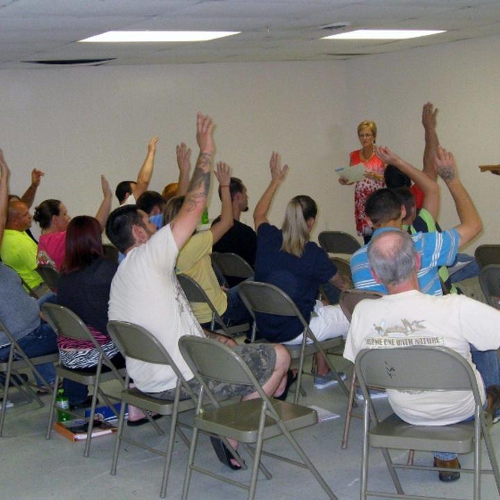 A group of people from court teams being led by an instructor, many with hands raised.